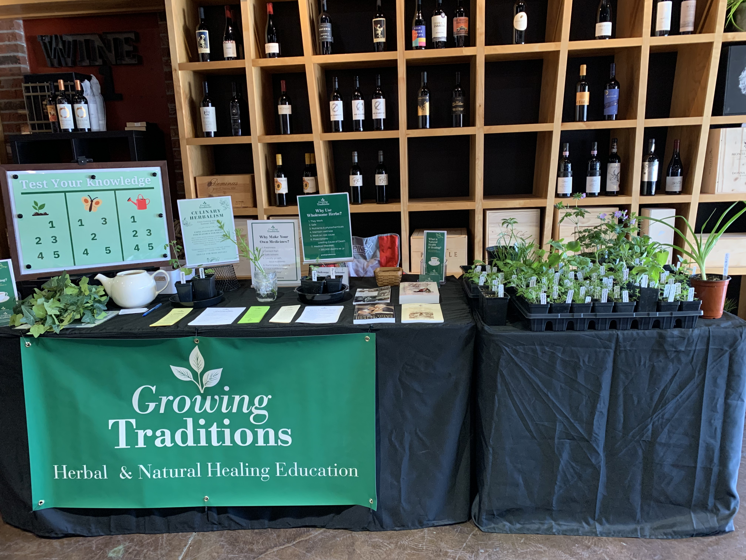 Herbal education booth at Sip N Shop featured a banner, trivia game, curated books, free herbal handouts and spring plant starts — herbs, vegetables and blooms.